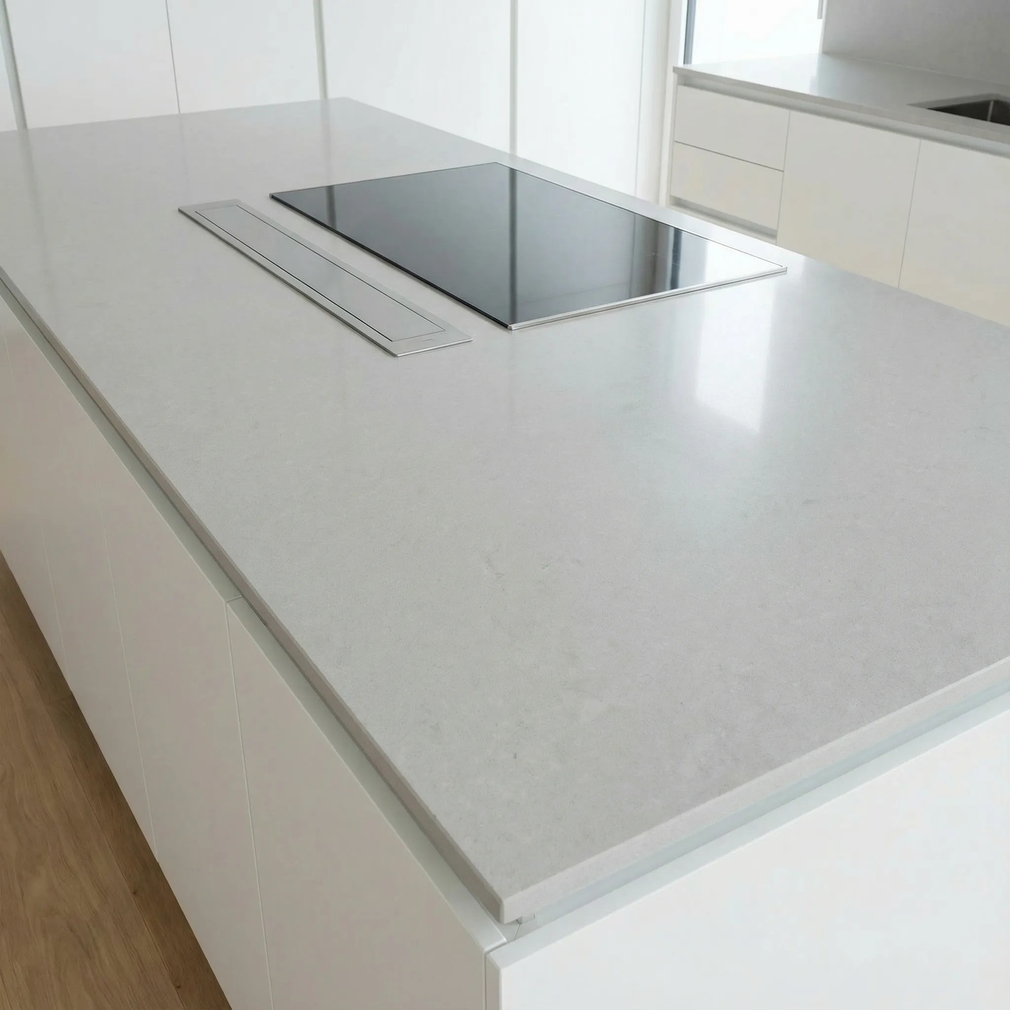 Detalj kuhinjskog ostrva sa svetlo sivom kvarcnom radnom pločom i integrisanom indukcijom