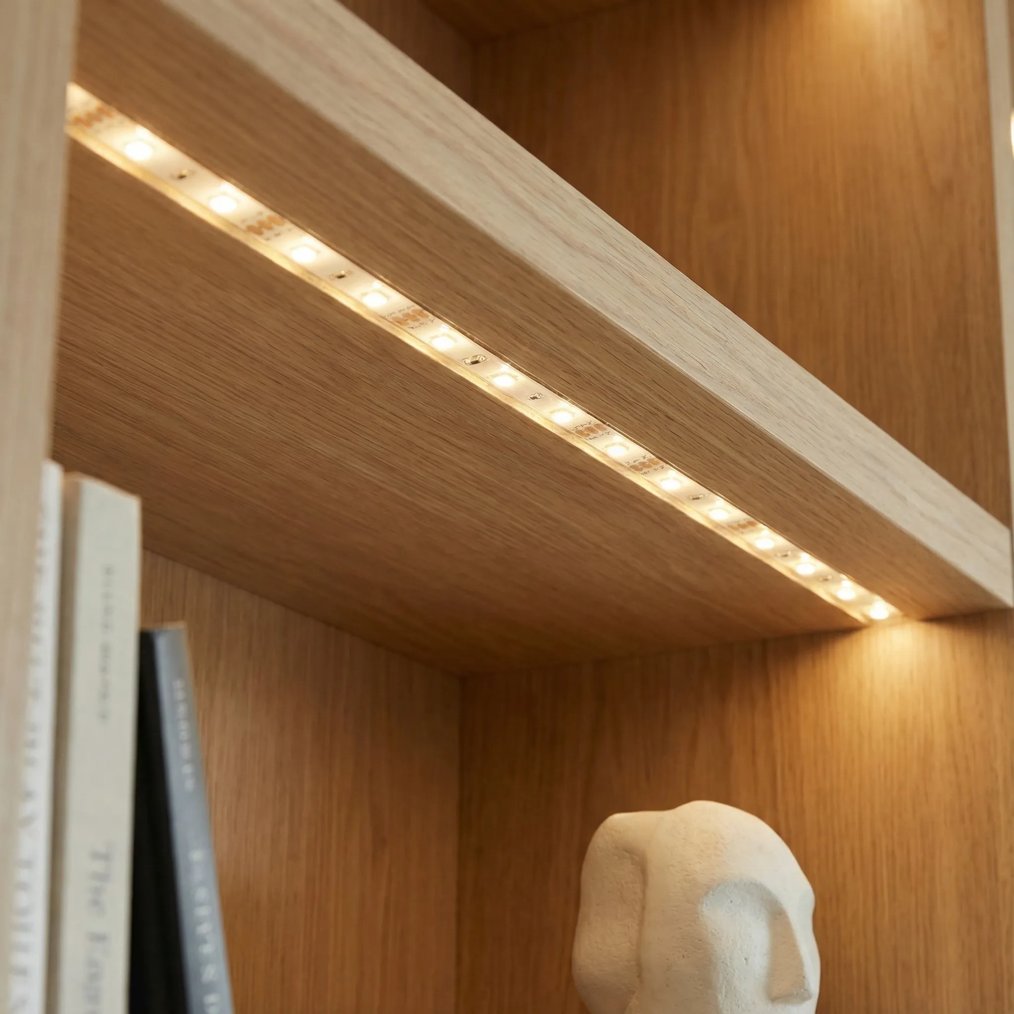Detalj LED trake ugrađene ispod police od hrasta sa skulpturom